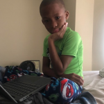 4th grader boy student with laptop sitting on bed,thinking